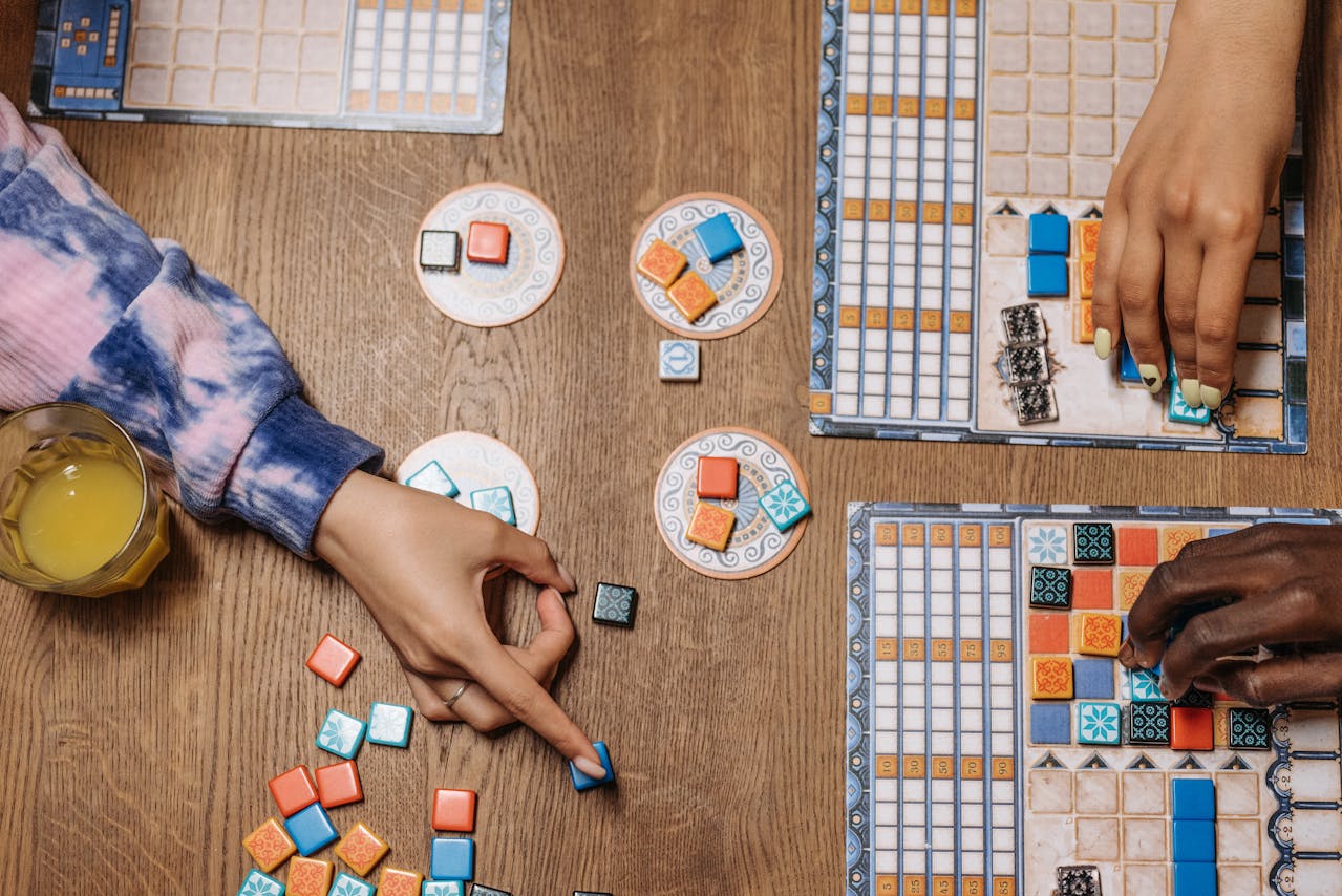 a table-top view of three people playing some of the most popular board games in 2024 image source: https://www.pexels.com/photo/hands-playing-board-games-8111328/