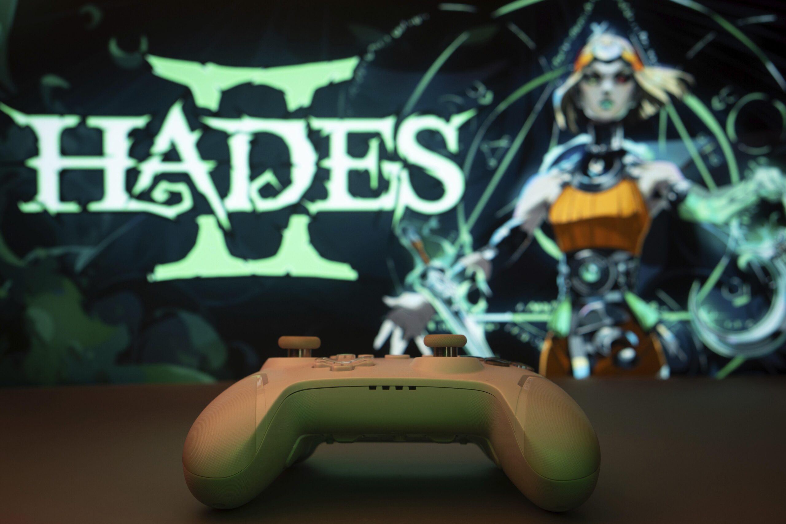 Hades II loaded on the screen with a green and white controller on the table in front